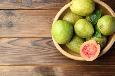 Fresh cut and whole guava fruits in bowl on wooden table, top view. Space for text