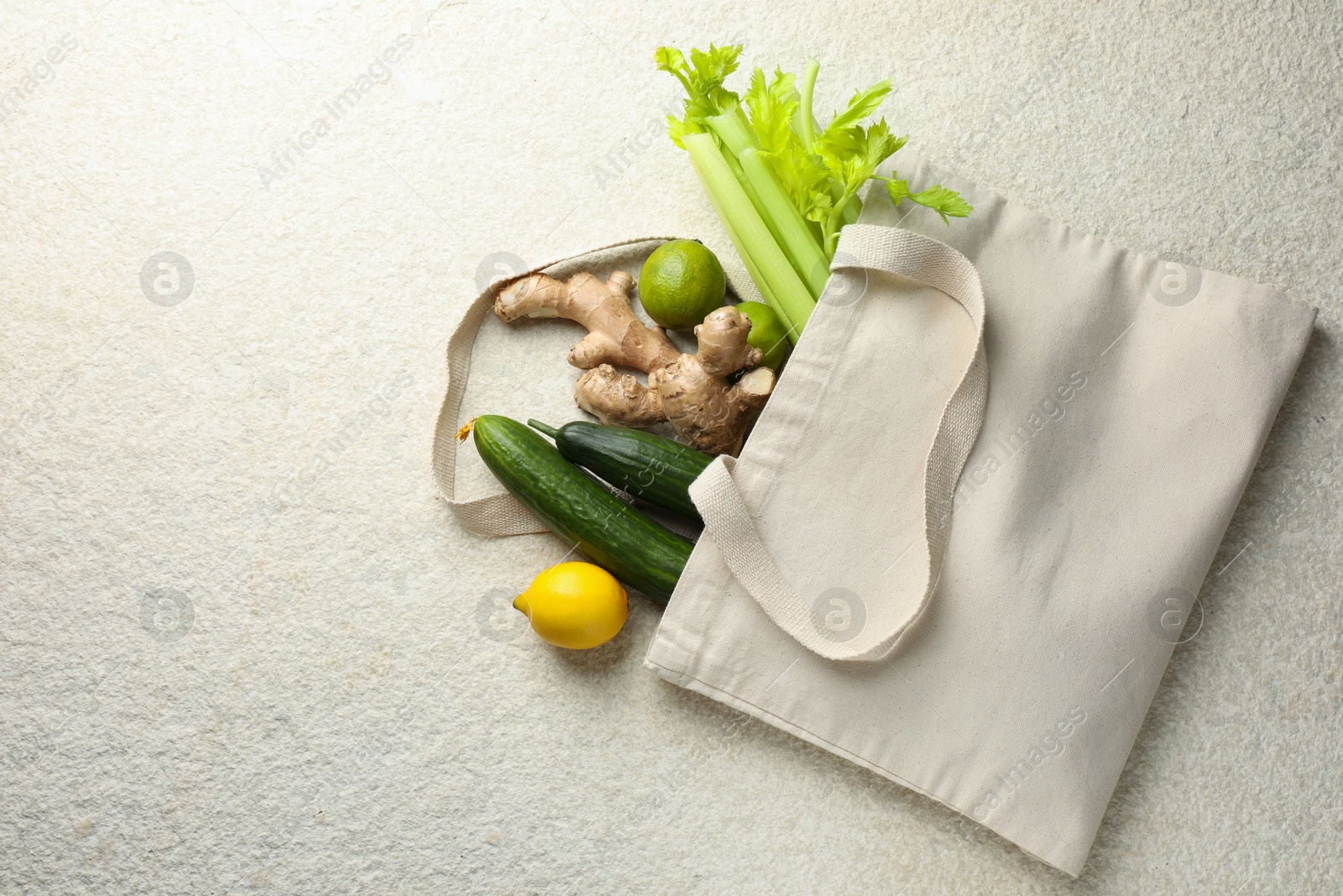 Photo of Eco bag with vegetables, fruits and ginger on white textured table, top view. Space for text