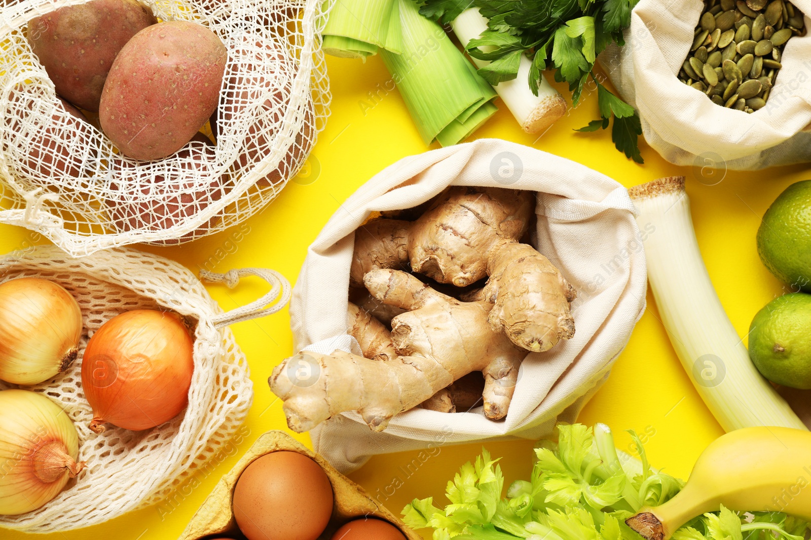 Photo of Eco bags with different food products on yellow background, flat lay