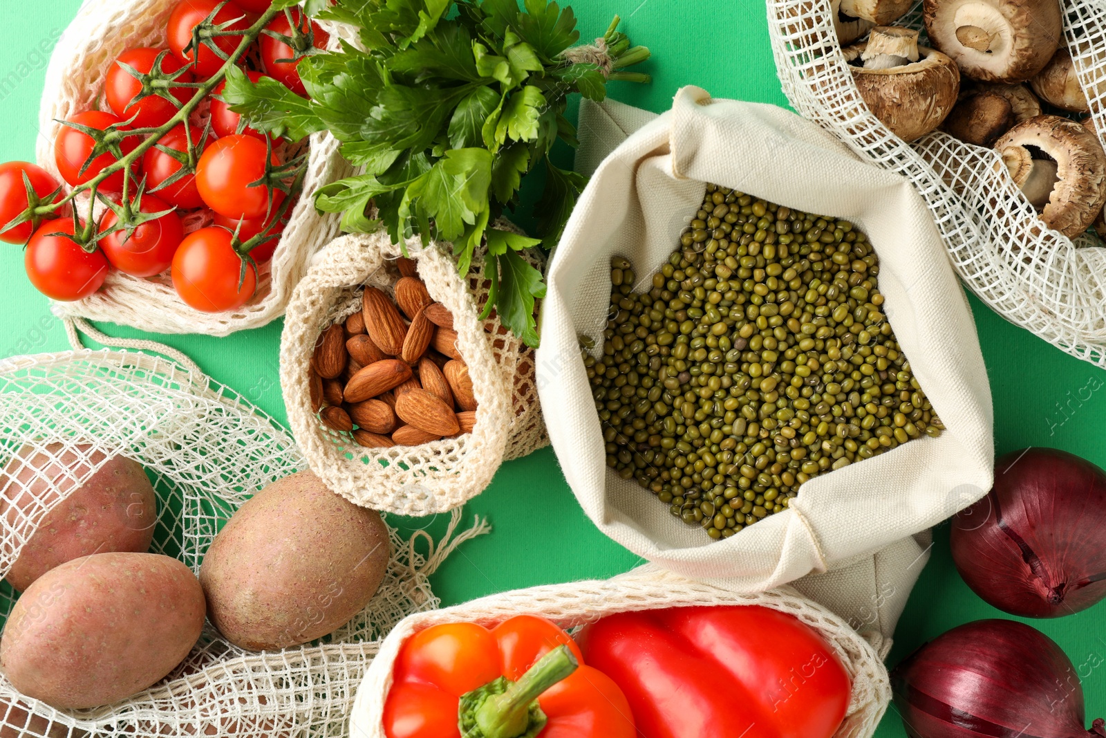 Photo of Eco bags with different food products on green background, flat lay