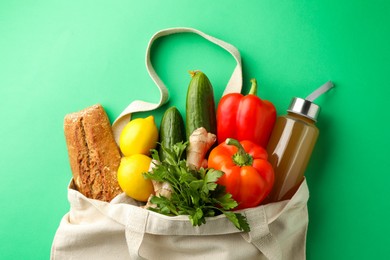 Photo of Eco bag with different food products and juice on green background, top view