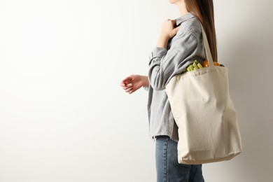 Photo of Woman holding shopper bag with groceries on white background, closeup and space for text. Eco friendly lifestyle