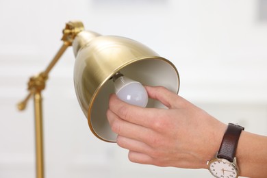 Photo of Man changing light bulb in lamp at home, closeup