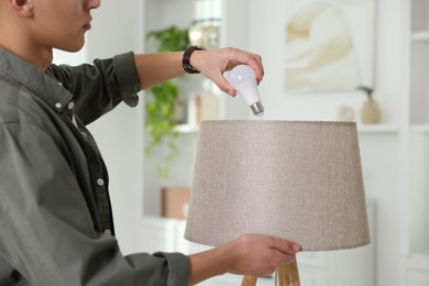 Photo of Man changing light bulb in lamp at home, closeup