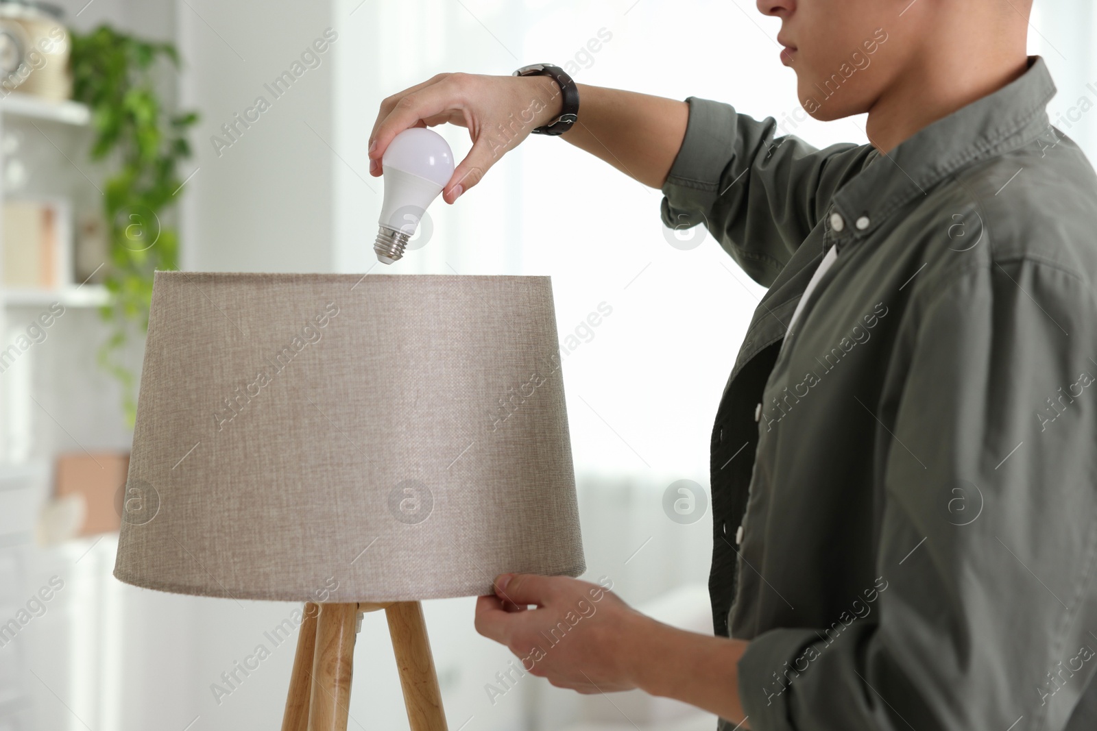 Photo of Man changing light bulb in lamp at home, closeup