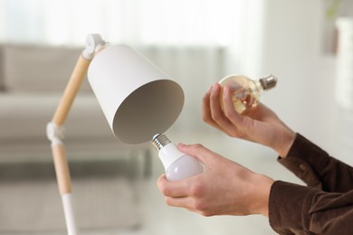 Photo of Man changing incandescent light bulb for fluorescent one in lamp at home, closeup