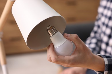 Photo of Man changing light bulb in lamp at home, closeup