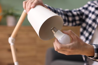 Photo of Man changing light bulb in lamp at home, closeup