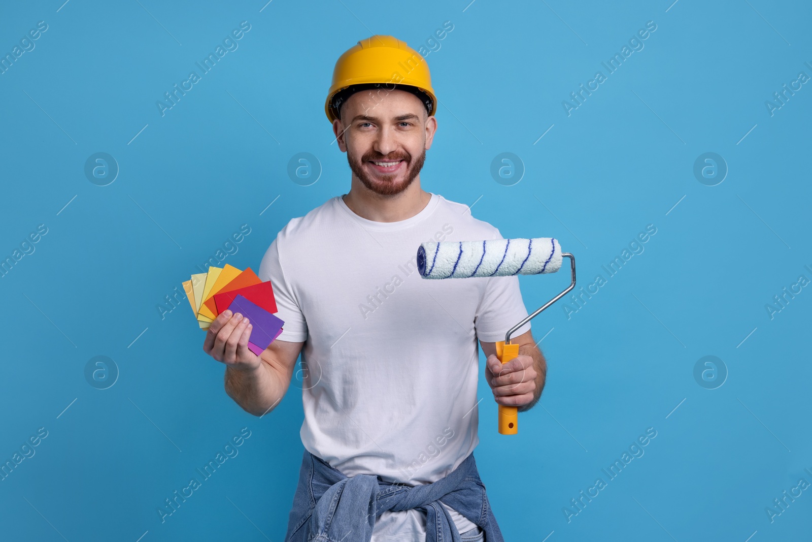 Photo of Man wearing hardhat with roller and color samples on blue background