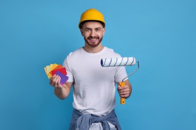 Man wearing hardhat with roller and color samples on blue background