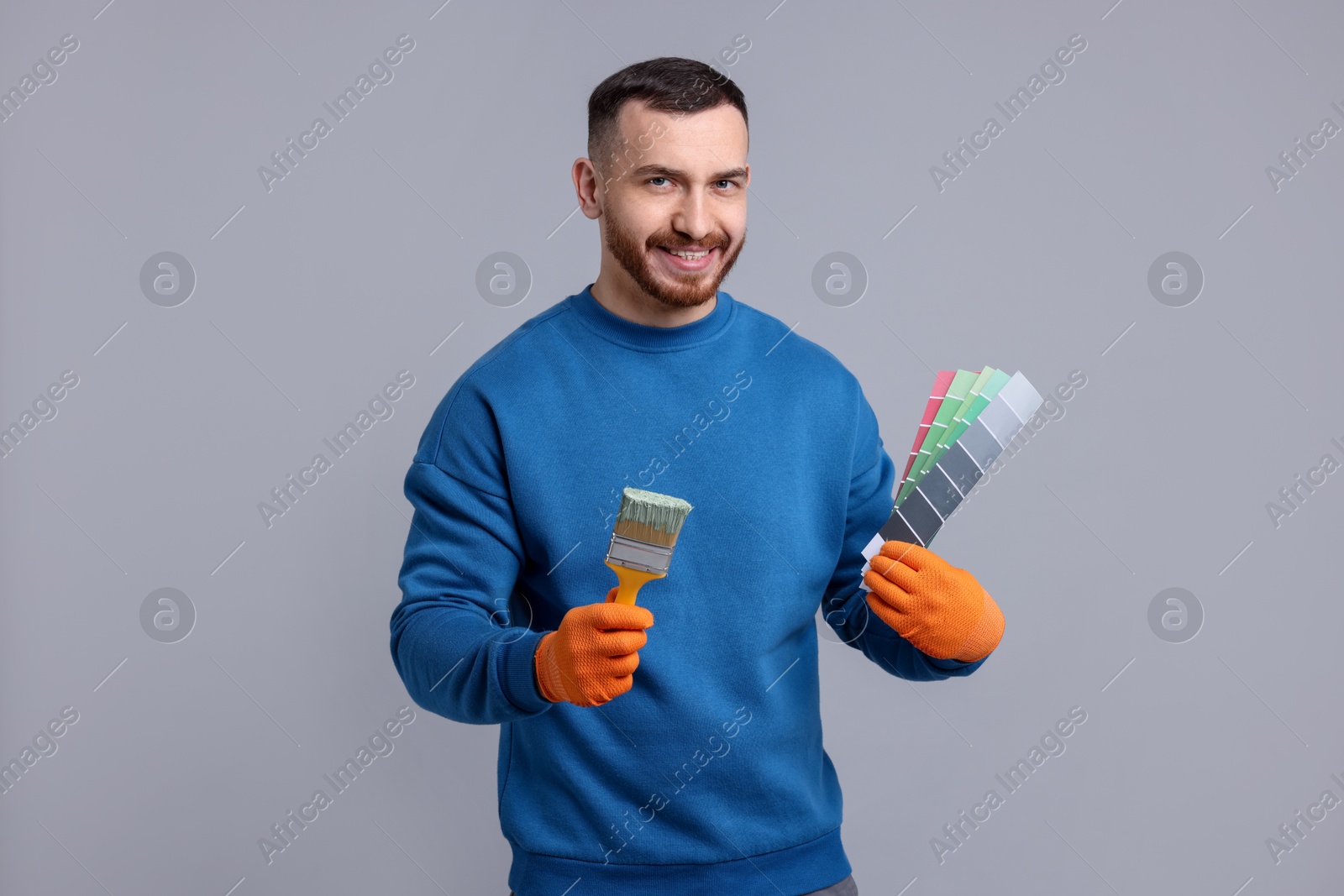 Photo of Man with paintbrush and color selection chart on light grey background