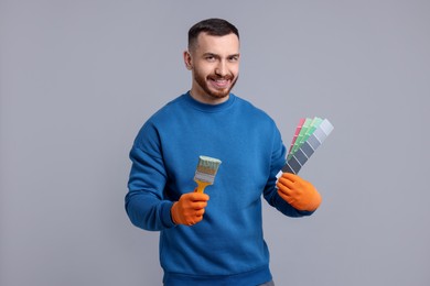 Man with paintbrush and color selection chart on light grey background