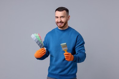 Photo of Man with paintbrush and color selection chart on light grey background