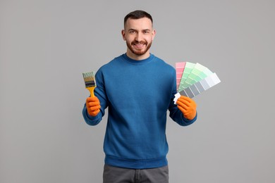 Photo of Man with paintbrush and color selection chart on light grey background