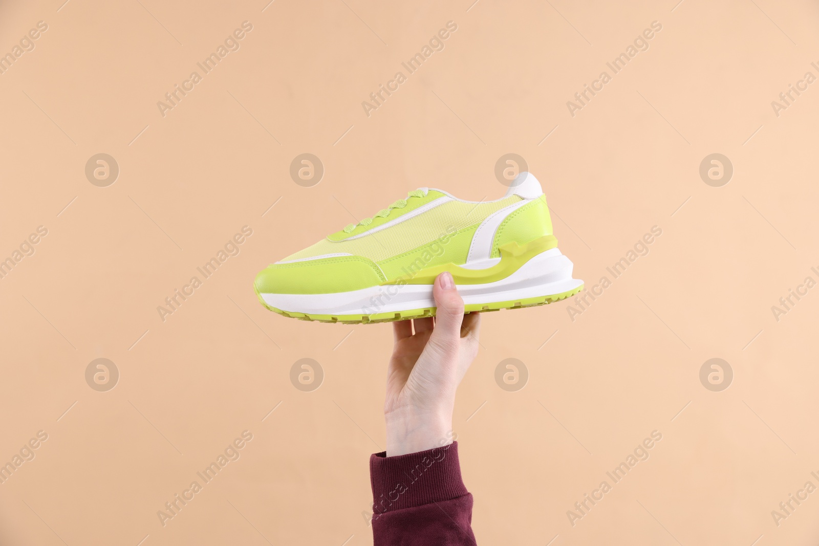 Woman with stylish sneaker on beige background, closeup Photo of Woman with stylish sneaker on beige background, closeup