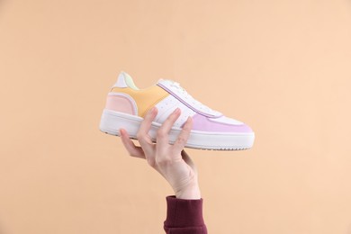 Woman with stylish sneaker on beige background, closeup