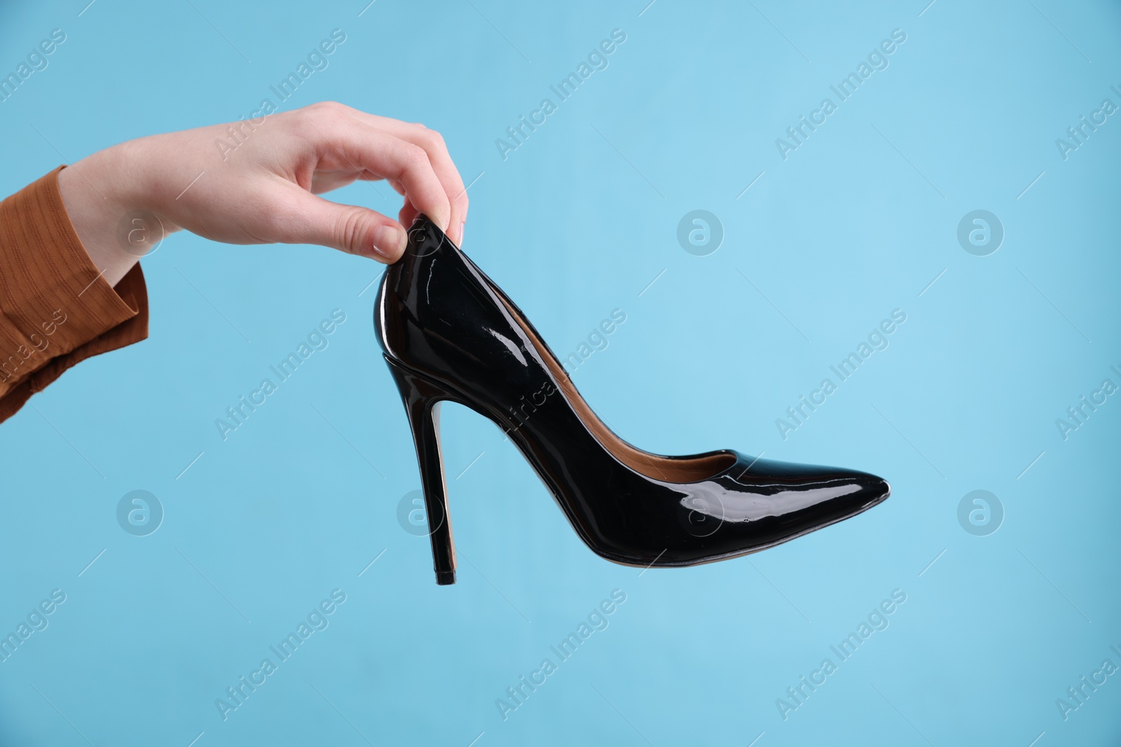 Photo of Woman with high heeled shoe on light blue background, closeup