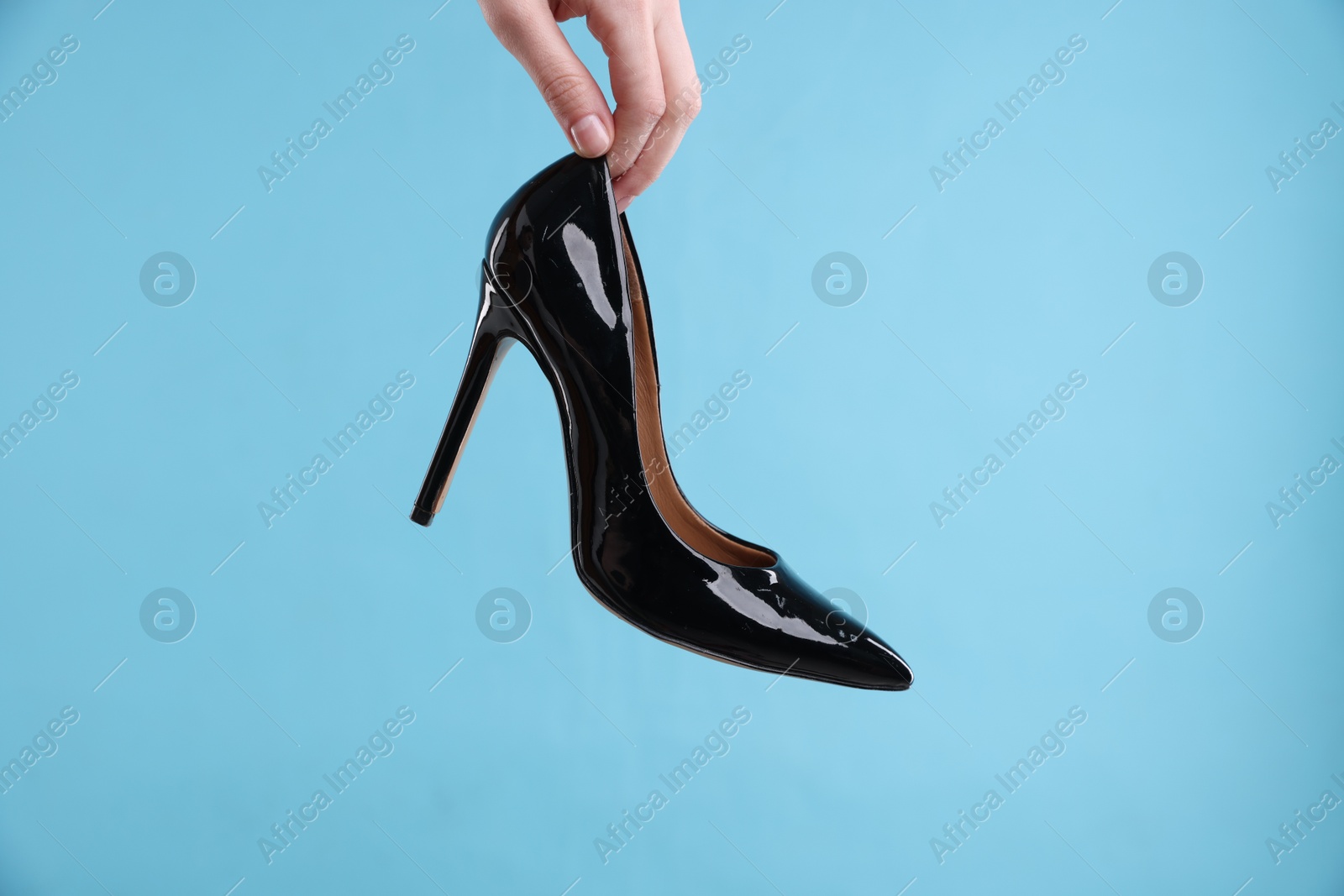 Photo of Woman with high heeled shoe on light blue background, closeup