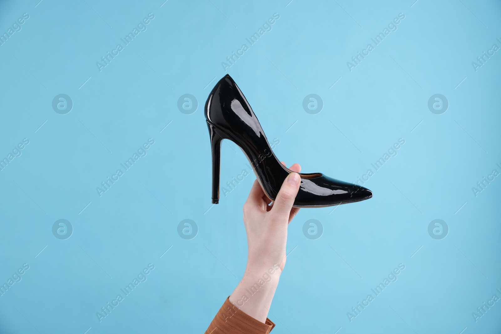 Photo of Woman with high heeled shoe on light blue background, closeup