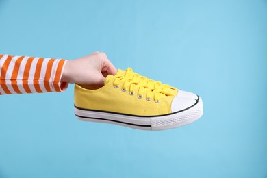 Woman with stylish sneakers on light blue background, closeup