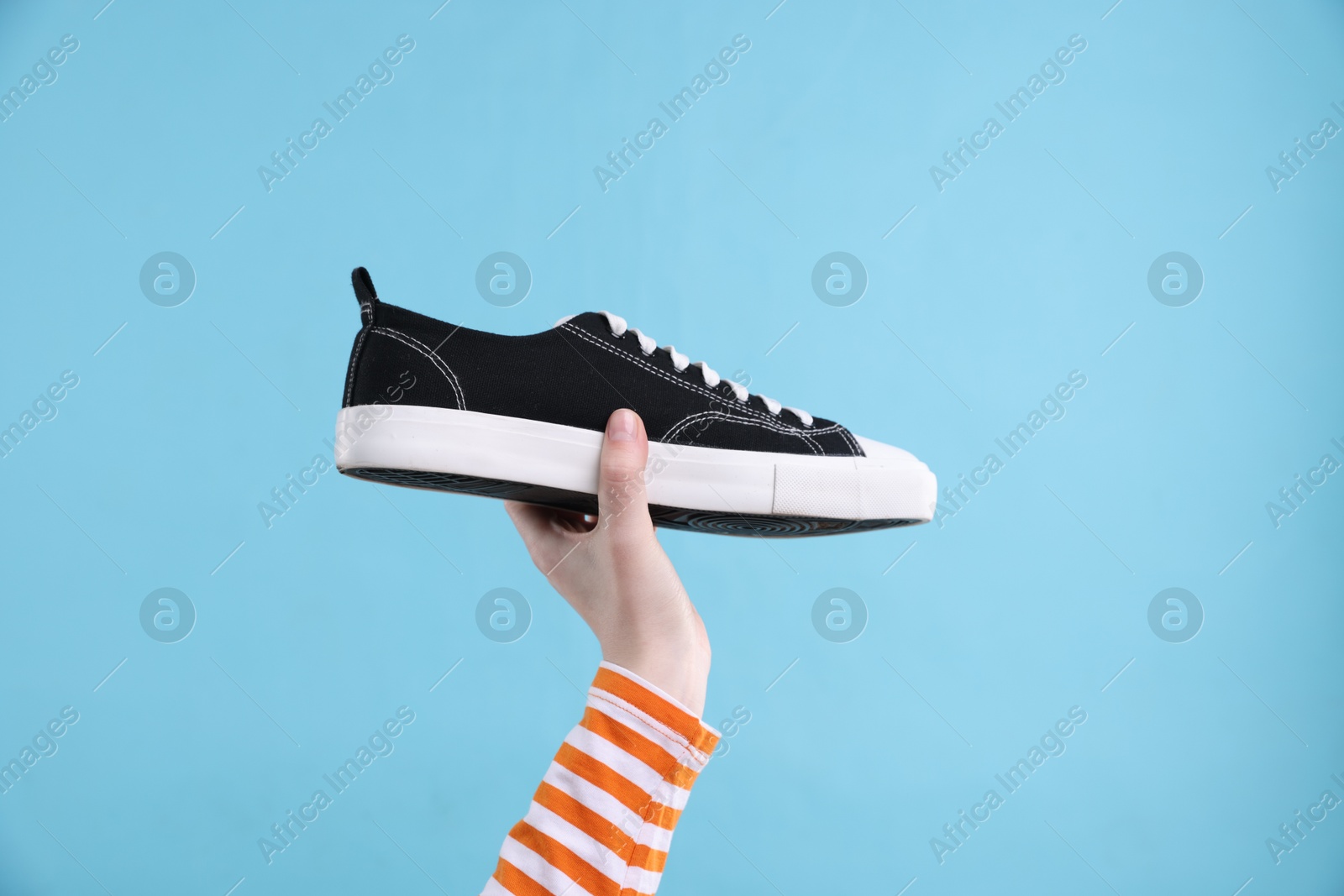 Photo of Woman with stylish sneaker on light blue background, closeup