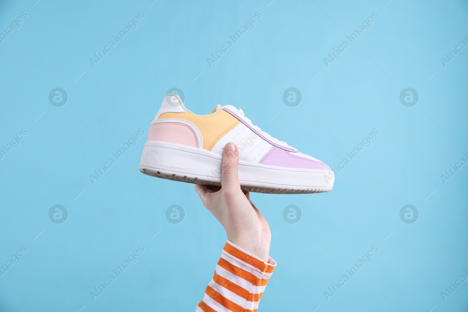 Photo of Woman with stylish sneaker on light blue background, closeup