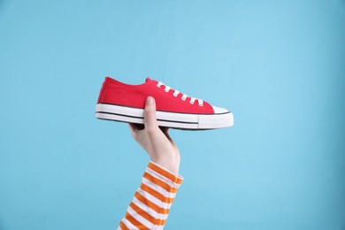 Woman with stylish sneaker on light blue background, closeup