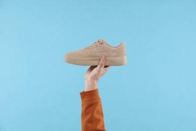 Man with stylish sneaker on light blue background, closeup