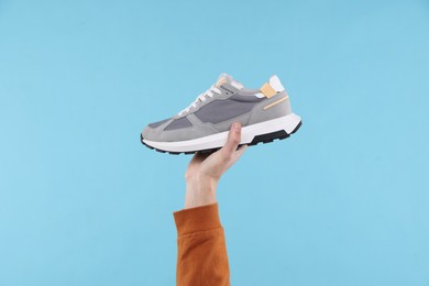 Man with stylish sneaker on light blue background, closeup