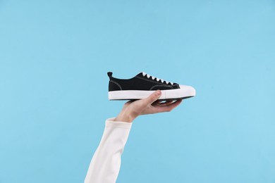 Man with stylish sneaker on light blue background, closeup