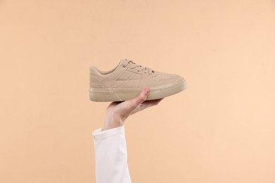 Man with stylish sneaker on beige background, closeup