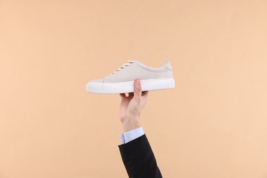 Man with stylish sneaker on beige background, closeup