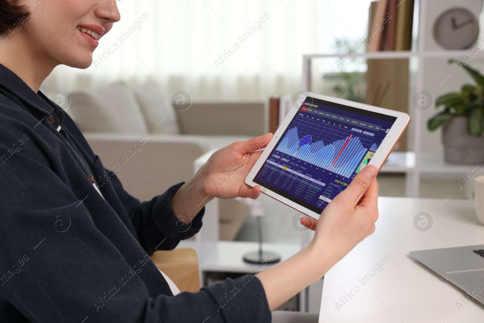 Photo of Stock exchange. Woman analysing financial market on tablet at white table indoors, closeup