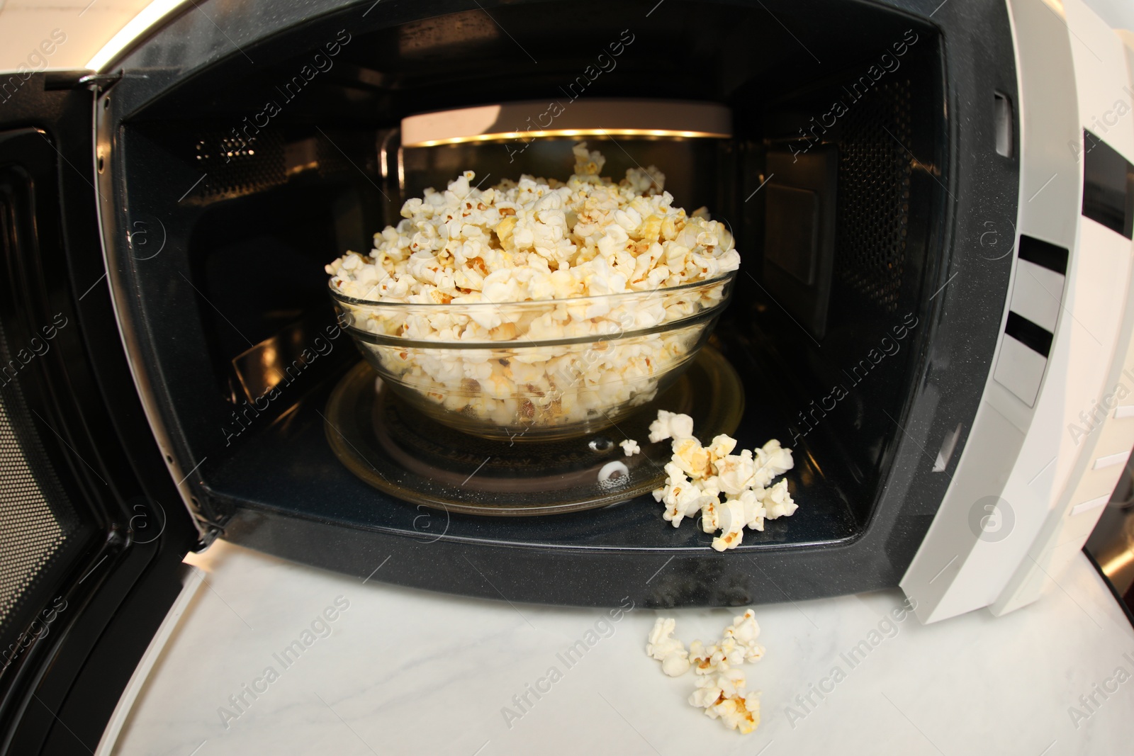 Photo of Bowl of tasty popcorn in microwave oven on white marble table, closeup. Fisheye lens effect