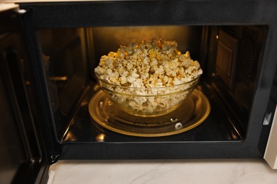 Photo of Bowl of tasty popcorn in microwave oven, closeup