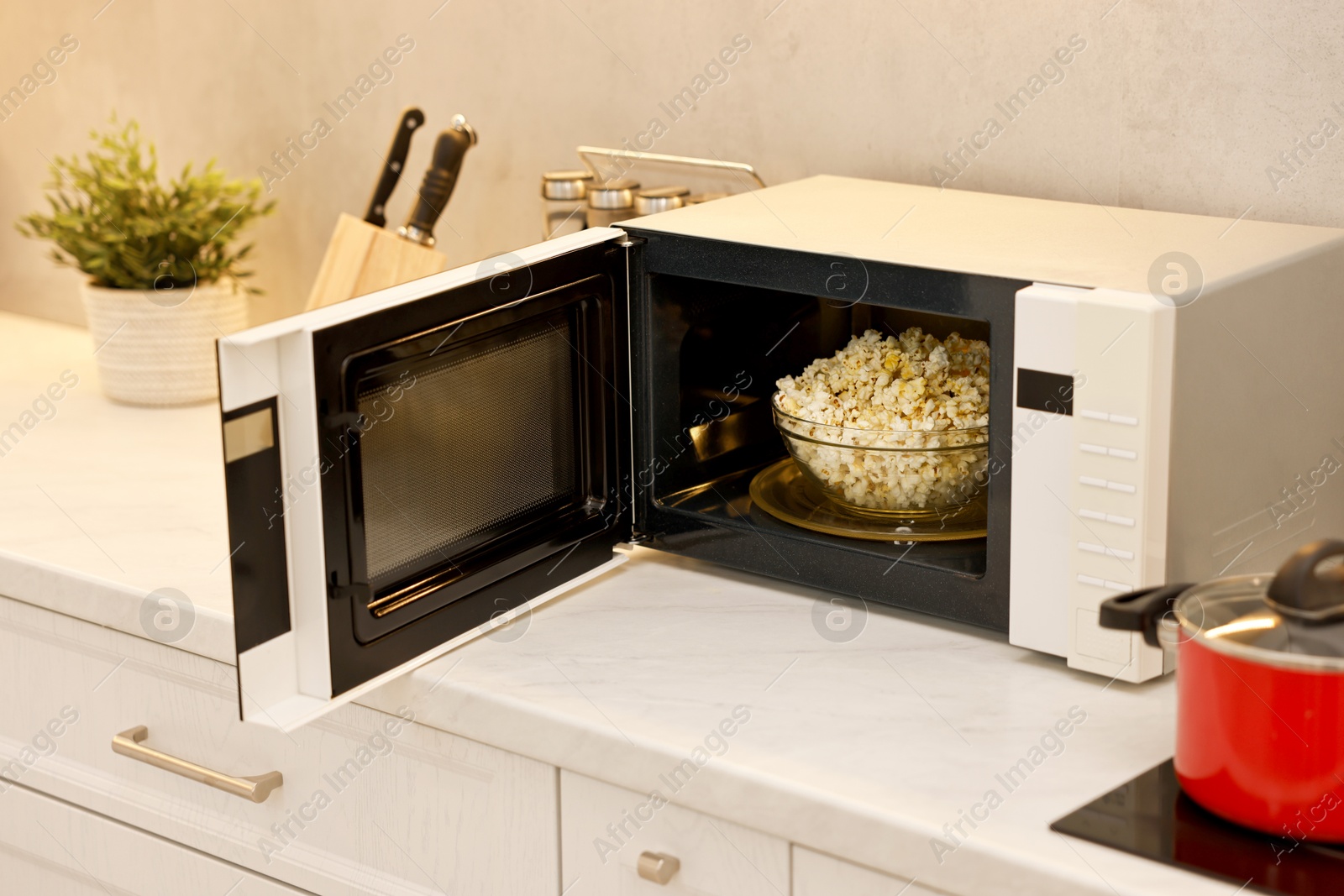 Photo of Open microwave oven with bowl of popcorn on white marble countertop in kitchen