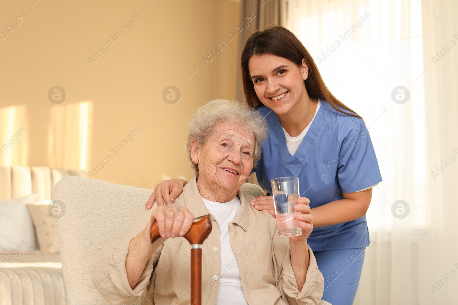 Photo of Healthcare worker and elderly woman with glass of water indoors