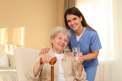 Photo of Healthcare worker and elderly woman with glass of water indoors