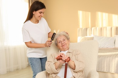 Granddaughter brushing her grandmother with comb at home. Elderly care