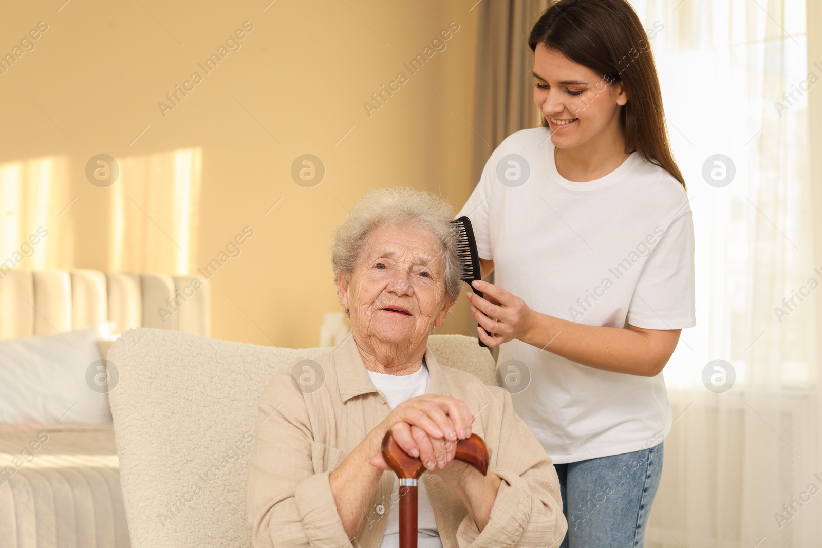 Photo of Granddaughter brushing her grandmother with comb at home. Elderly care