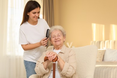 Photo of Granddaughter brushing her grandmother with comb at home. Elderly care