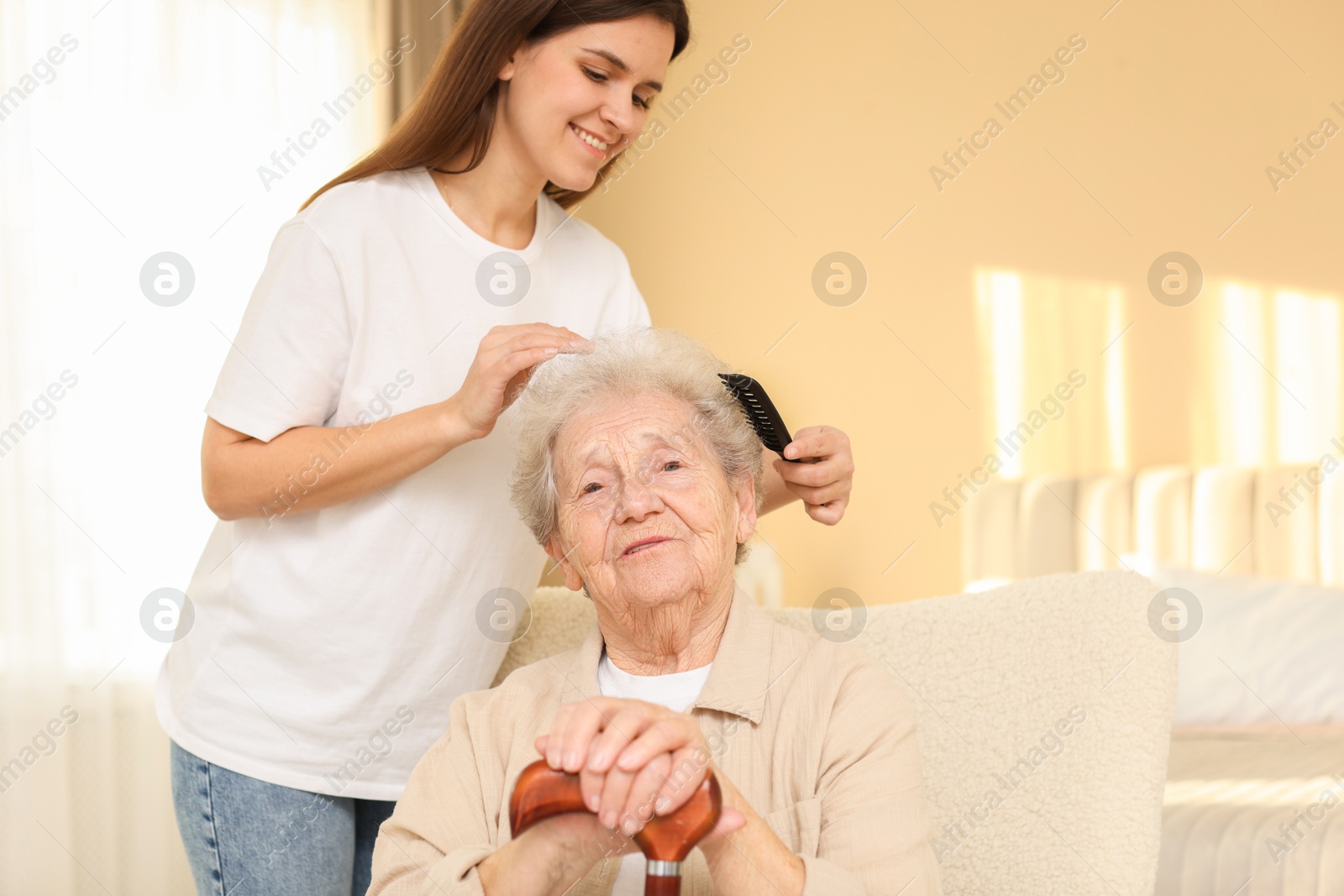 Photo of Granddaughter brushing her grandmother with comb at home. Elderly care