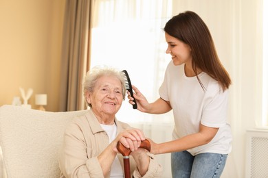 Photo of Granddaughter brushing her grandmother with comb at home. Elderly care