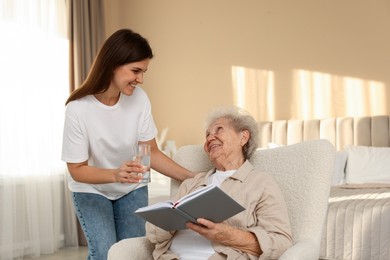 Photo of Granddaughter giving glass of water to her grandmother at home. Elderly care