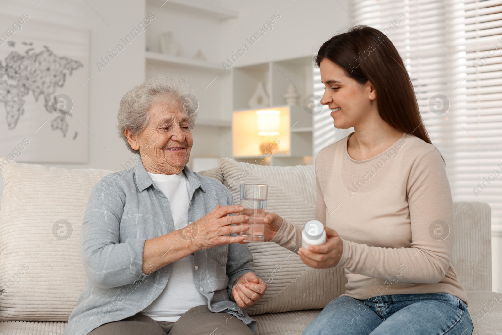 Photo of Granddaughter giving pills and glass of water to her grandmother at home. Elderly care