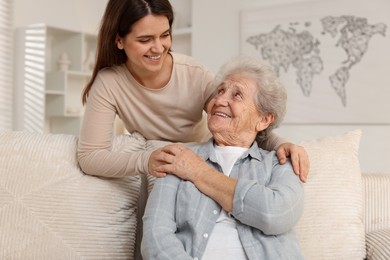 Photo of Happy granddaughter with her grandmother on sofa at home. Elderly care