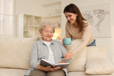 Photo of Granddaughter giving hot drink to her grandmother at home. Elderly care