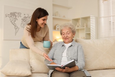 Photo of Granddaughter giving hot drink to her grandmother at home. Elderly care