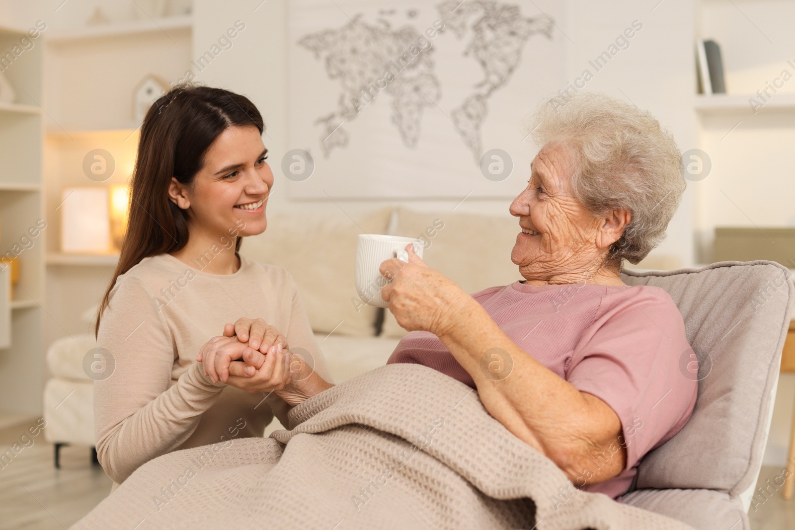 Photo of Granddaughter giving hot drink to her grandmother at home. Elderly care