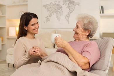 Granddaughter giving hot drink to her grandmother at home. Elderly care